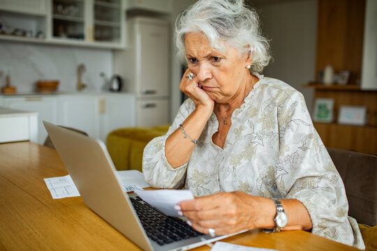 Concerned senior woman reviewing bills on laptop at home