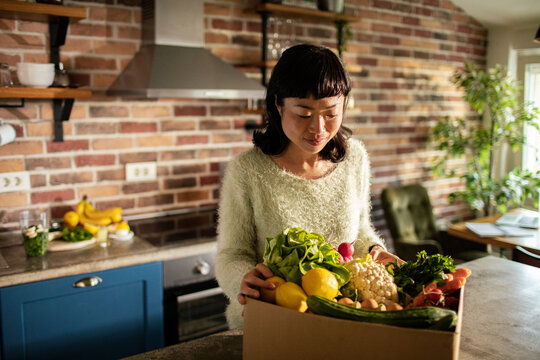 Woman unpacking fresh produce in home kitchen