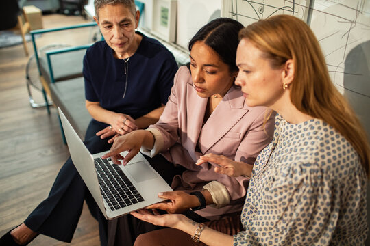 Three businesswomen collaborating on laptop in modern office