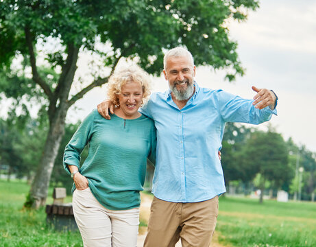 Happy active middle aged white couple having fun walking holding hands and bonding in park outdoors