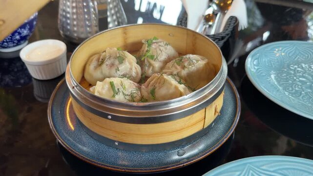 Steamed dumplings filled with meat and herbs served hot in a traditional bamboo steamer. Appetizing Asian-style dumplings garnished with fresh dill in a restaurant