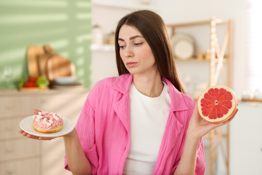 Healthy diet. Woman choosing between donut and half of grapefruit indoors