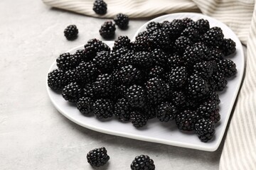 Many fresh blackberries and heart shaped plate on grey textured table, closeup © New Africa