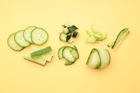 Different cuts of cucumbers on yellow background, flat lay