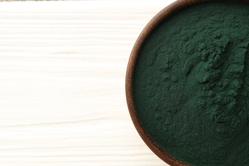 Obraz premium Spirulina powder in bowl on white wooden table, top view. Space for text
