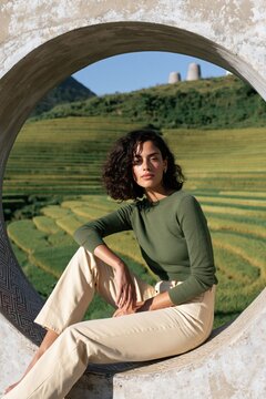 Woman sitting in circular stone frame with terraced green rice fields background for outdoor lifestyle portrait and travel lifestyle