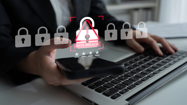 A businessman uses a smartphone while working on a laptop in an office setting, highlighting the seriousness of data breach warnings in today digital environment. Ledger