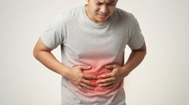 Young man holding abdomen in pain indicating digestive issues or stomach discomfort while standing against isolated grey backdrop.