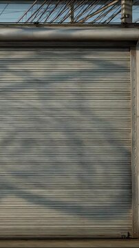 Rolling metal garage shutter door featuring shifting shadows and light movement in this smooth industrial video