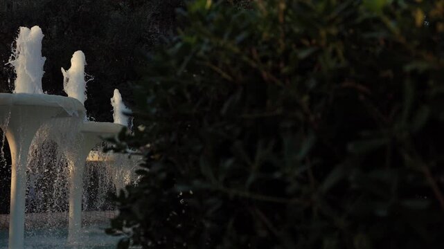 Cinematic pan revealing a splashing white tiered fountain in a city park