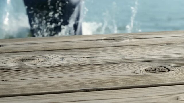 Bare feet push off a sunlit wooden dock and jump into calm blue water, leaving the weathered boards behind as a bright splash rises against the softly blurred waterside background