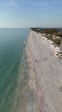 Still shot of a couple walking their dogs on a nearly empty sandy beach at Casey Key, a barrier island, in Sarasota County, Florida. 