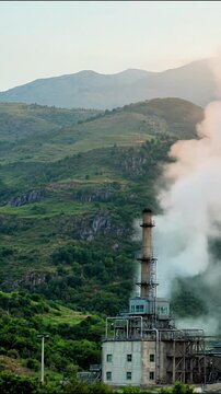 Industrial geothermal plant emitting steam amidst lush green mountain landscape in high resolution motion video footage