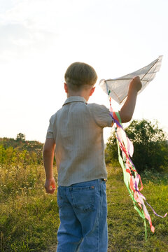 Child holding a handmade kite with colorful ribbons against the sky