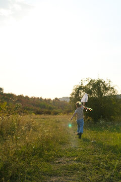 Boy running with a handmade kite raised in the air on a summer evening