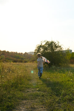 Boy running with a handmade kite in nature on a summer evening