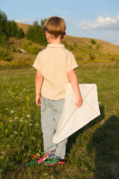Child holding a handmade white kite outdoors on a summer evening