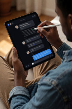Man uses stylus on tablet interacting with AI chatbot. He learns about CRM system implementation at home. Digital communication and business strategy at home office.