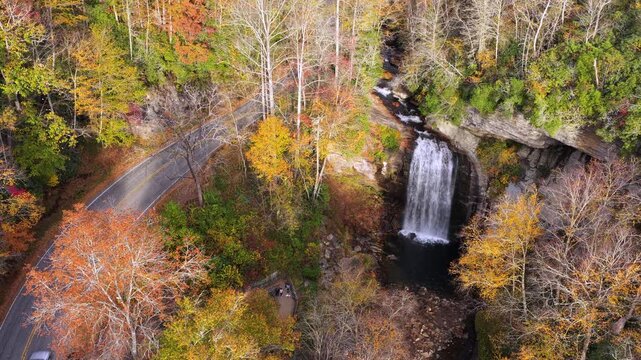 Scenic aerial landscape featuring mountain waterfall, viewing platform and forest staircase. Colorful autumn trees frame cascading water and visiting tourists.