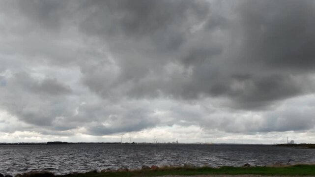 High contrast view of overcast low-hanging clouds over the Limfjord water with distant wind turbines on a cloudy day