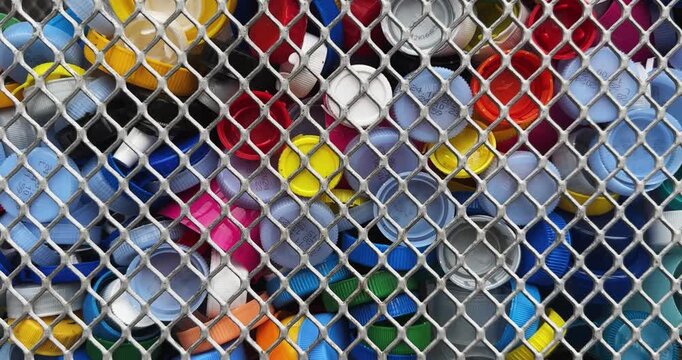 A pile of plastic caps are stacked in a cage. The caps are of different colors and sizes, recycling concept shot