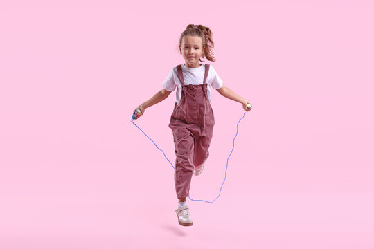 Cute little girl jumping with skipping rope on pink background