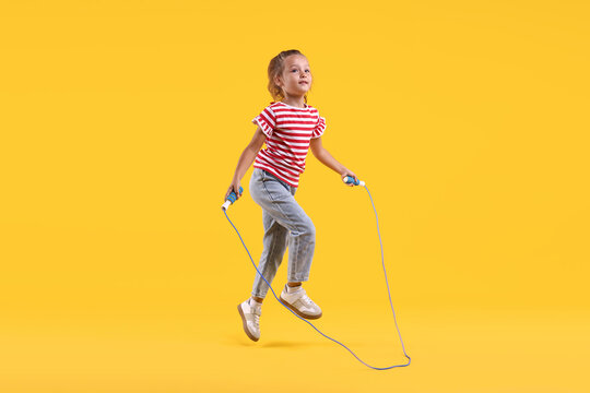 Cute little girl jumping with skipping rope on yellow background