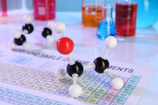 Chemical model of ethanol molecule, periodic table and laboratory glassware on white table, closeup