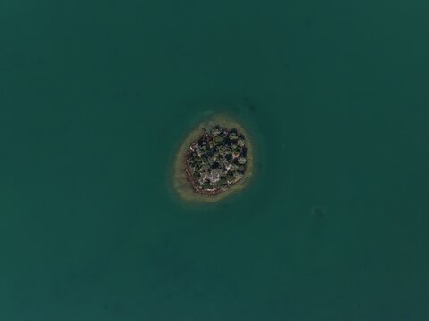 Aerial top-down view of a tiny isolated green island in the middle of a vast dark green lake.