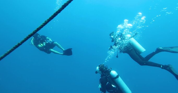 A group of divers diving towards a sunken ship in the Philippine Sea. Divers descend together around a guide rope. Divers descend into a cloud of bubbles. Summer vacation shot