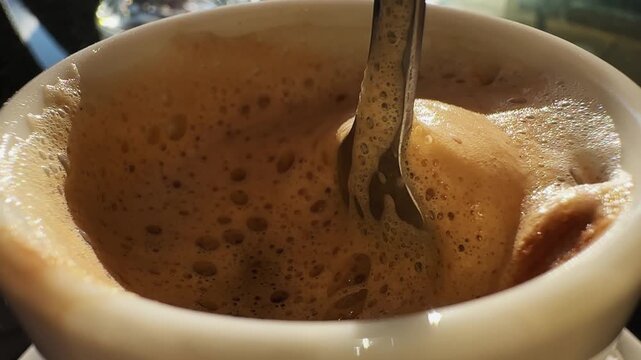 A white coffee cup with foam on top and a spoon in it. The foam is brown and the cup is almost empty
