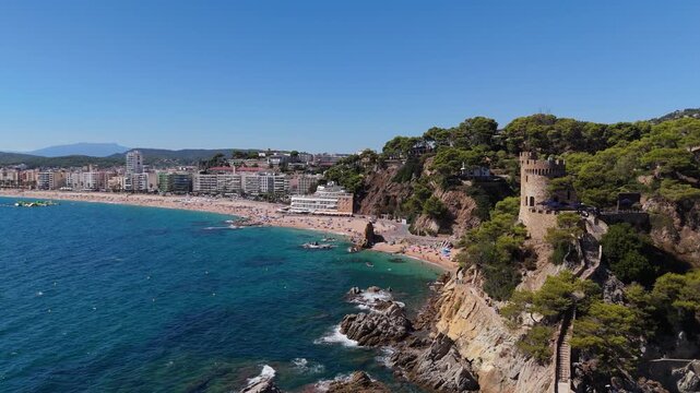 Aerial view of the coastline of Lloret de Mar, Costa Brava, Spain, filmed with a drone - the sea, beach, and castle on the coastal cliffs of the city bay on a sunny day