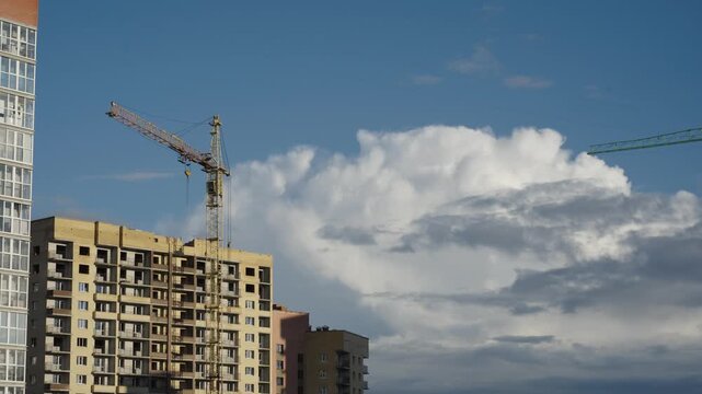 Construction cranes operate next to apartment facades under dramatic cloud formations Natural daylight creates shadows and highlights across brick surfaces and window glass Shots include close ups of 