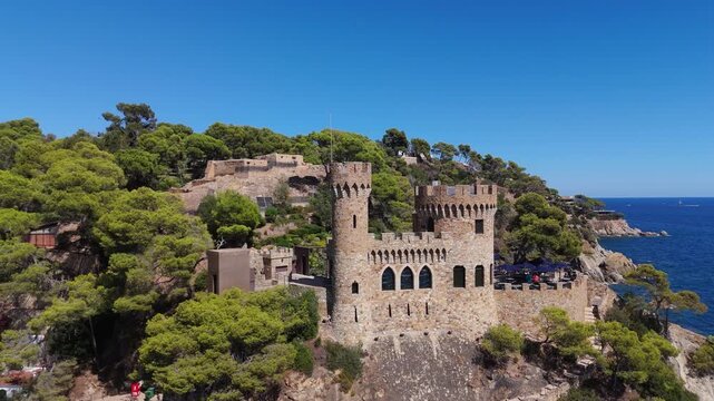 Aerial view of the coastline of Lloret de Mar, Costa Brava, Spain, filmed with a drone - the sea, beach, and castle on the coastal cliffs of the city bay on a sunny day