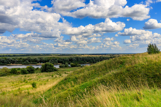 Vast landscape with grassy hill, river, and fluffy clouds