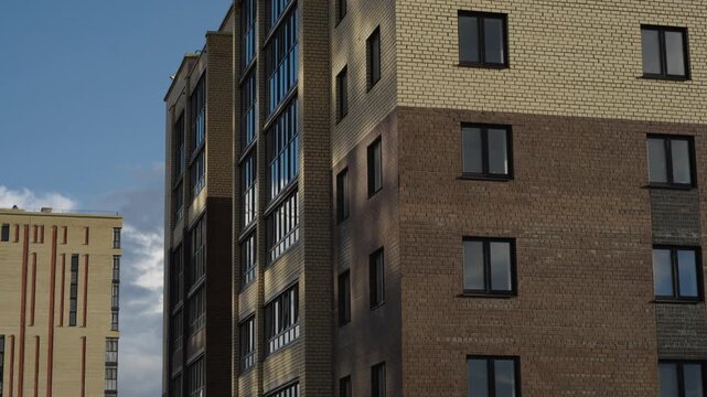 Construction cranes operate next to apartment facades under dramatic cloud formations Natural daylight creates shadows and highlights across brick surfaces and window glass Shots include close ups of 