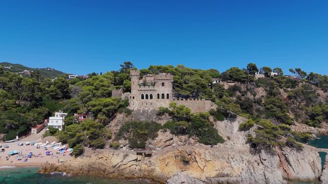 Aerial view of the coastline of Lloret de Mar, Costa Brava, Spain, filmed with a drone - the sea, beach, and castle on the coastal cliffs of the city bay on a sunny day