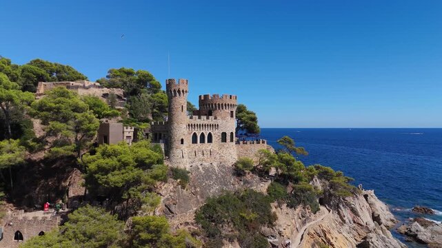 Aerial view of the coastline of Lloret de Mar, Costa Brava, Spain, filmed with a drone - the sea, beach, and castle on the coastal cliffs of the city bay on a sunny day