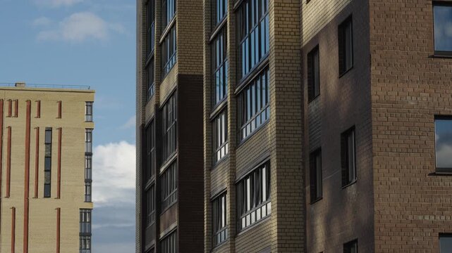 Construction cranes operate next to apartment facades under dramatic cloud formations Natural daylight creates shadows and highlights across brick surfaces and window glass Shots include close ups of 