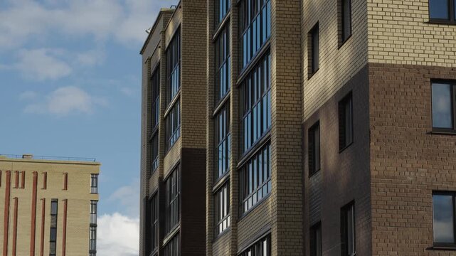 Construction cranes operate next to apartment facades under dramatic cloud formations Natural daylight creates shadows and highlights across brick surfaces and window glass Shots include close ups of 
