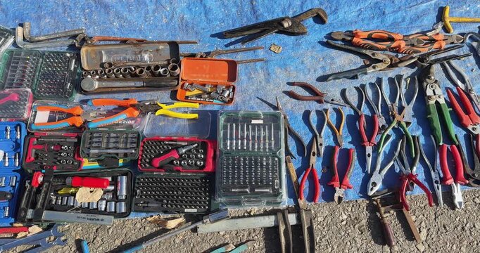 A pile of tools and equipment are scattered on the ground. The tools include wrenches, pliers, and other assorted items. The scene is chaotic and disorganized