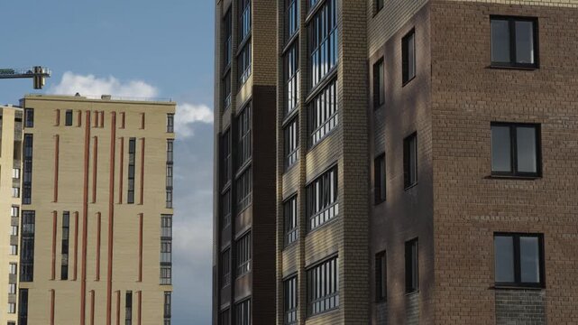 Construction cranes operate next to apartment facades under dramatic cloud formations Natural daylight creates shadows and highlights across brick surfaces and window glass Shots include close ups of 