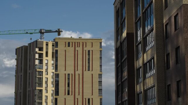 Construction cranes operate next to apartment facades under dramatic cloud formations Natural daylight creates shadows and highlights across brick surfaces and window glass Shots include close ups of 