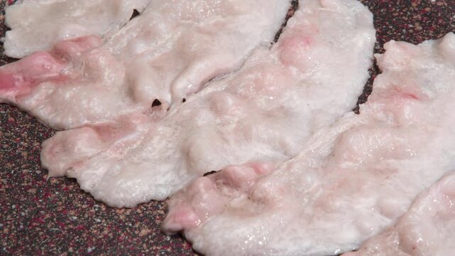 Crispy-fried Bacon Strips. Time Lapse. Raw bacon strips are fried until golden in a non-stick frying pan