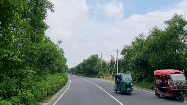 Two three-wheeled vehicles traveling along a scenic country road flanked by dense trees
