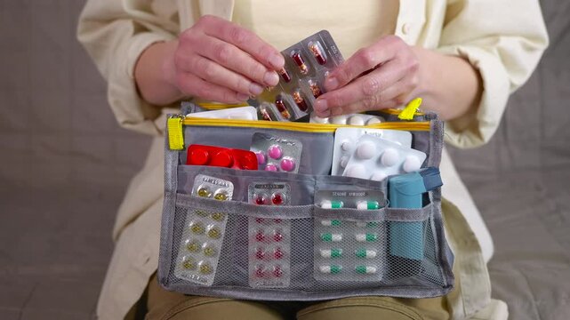 Woman organizing medication into first aid kit. Female hands carefully arranging various blister packs of pills, capsules, and an inhaler into a gray portable medicine organizer bag, for travel