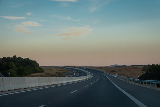 A curving stretch of Slovakia's R2 motorway near Zvolen sweeps through open farmland at dusk, with distant hills and soft pastel sky colors marking the fading daylight.