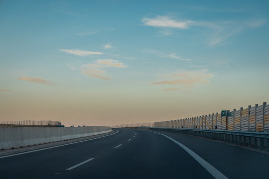 A curving stretch of Slovakia's R2 motorway near Zvolen sweeps through open farmland at dusk, with distant hills and soft pastel sky colors marking the fading daylight.