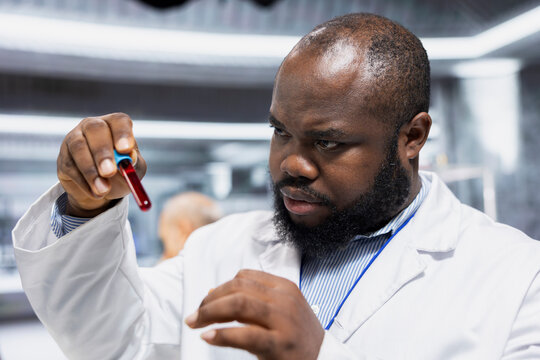 Black male scientist reviews a blood test sample during a laboratory experiment, collecting pharmacology data and recording reactions for product development and innovation in medical research.