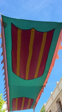 Festive green street canopy decorated with the Senyera Valencian heraldic shield banner stretched above a street in Lliber, Spain. Low angle view of traditional festival shade awning waving gently aga